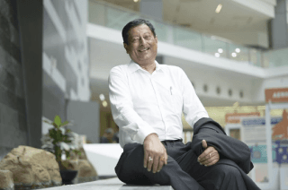 Man sitting on a bench in a shopping centre, hands on knees and relaxedly leaning back and laughing