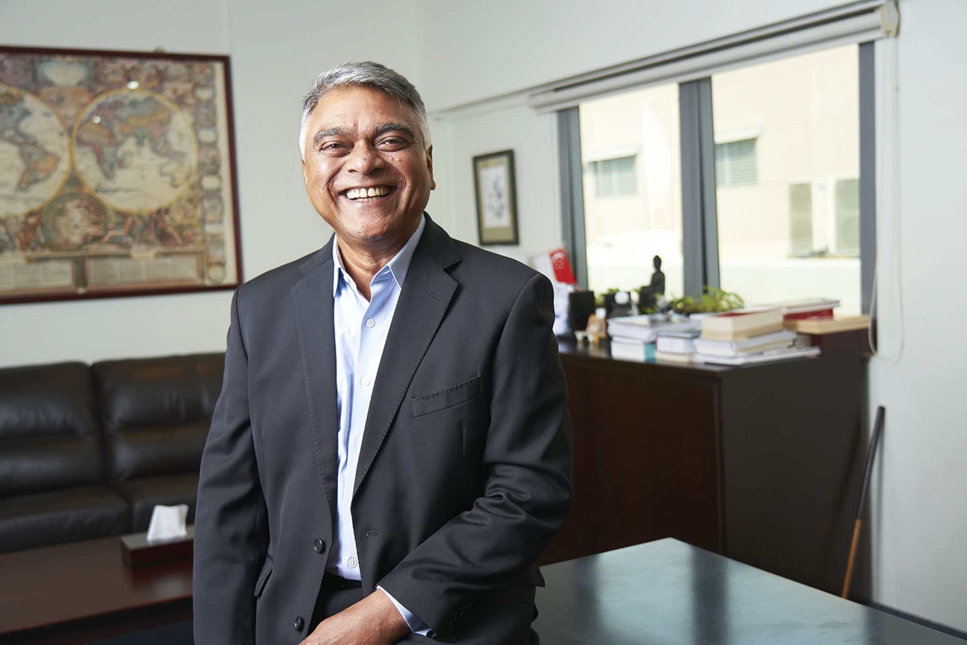 Businessman smiling happily, leaning against a desk in a corporate office